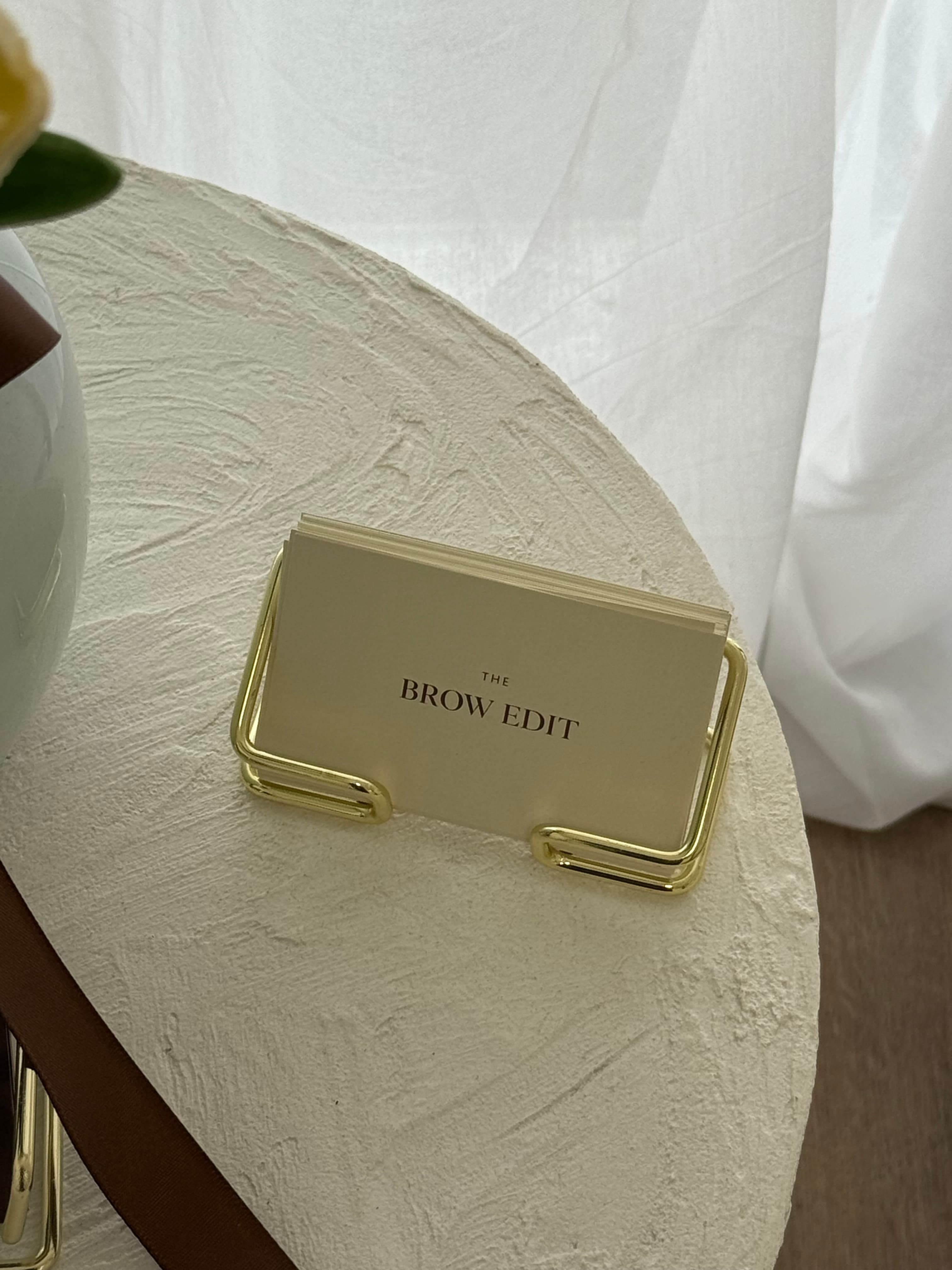 The Brow Edit business cards resting in a gold holder on a textured stone tray